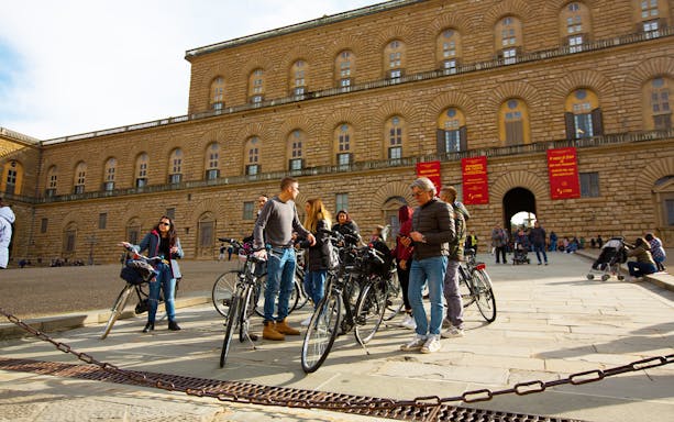 Cyclists gathered at Piazza Pitti in Florence, Italy, with the historic palace in the background.