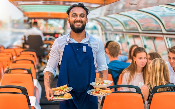 Service staff on a dinner cruise serving meals to guests on a boat.
