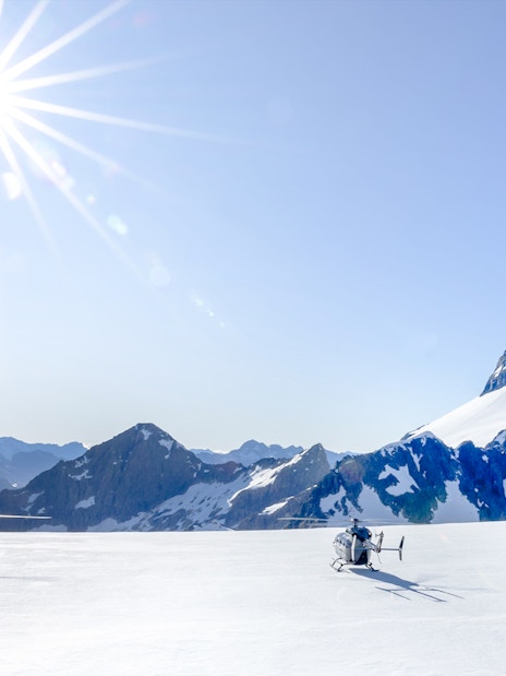 Two helicopters on a snow-covered glacier in the Southern Alps, Queenstown, under a bright sun.