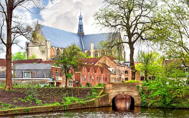 Alkmaar canal with historic church and brick bridge surrounded by lush greenery.