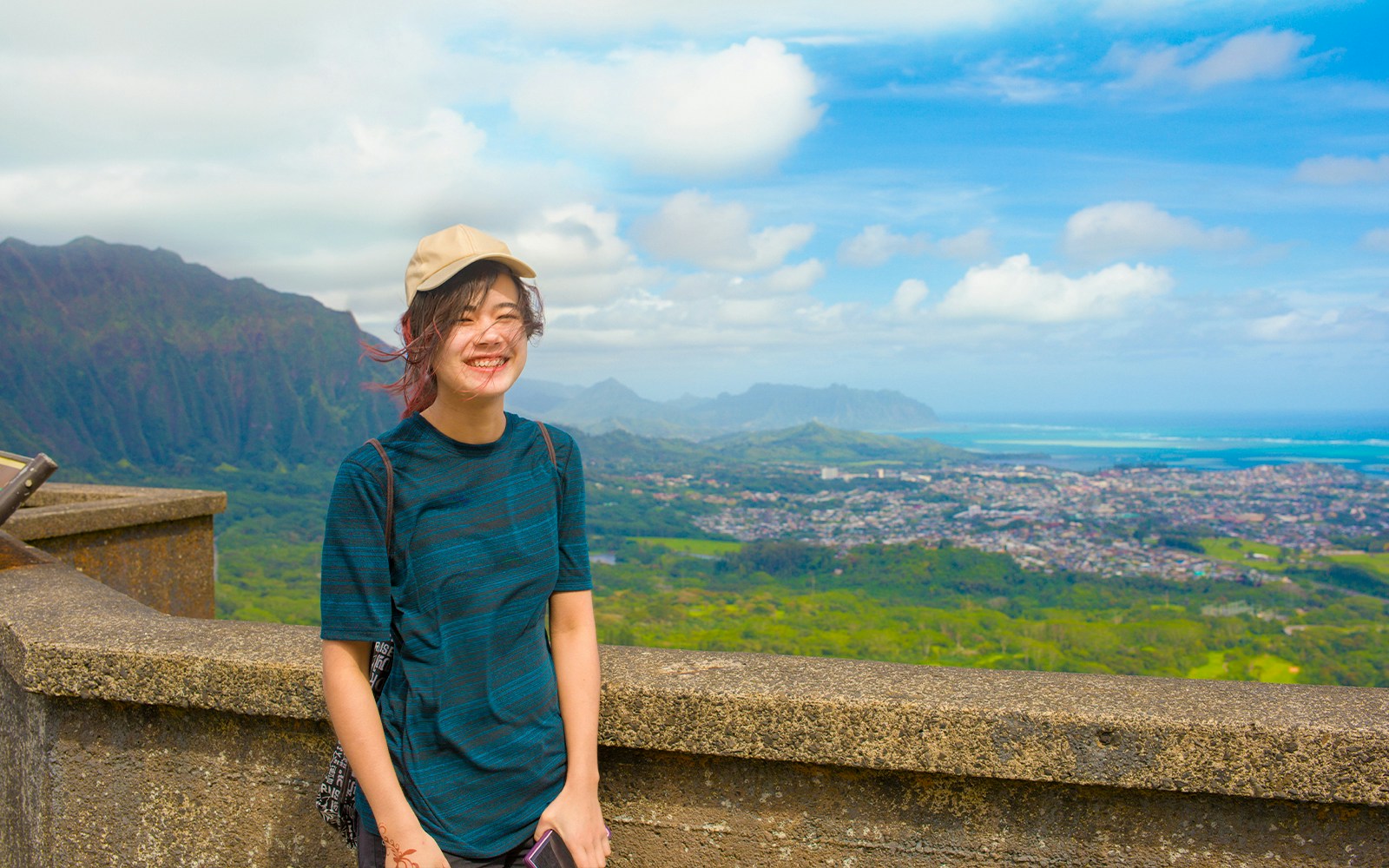 Girl smiling at Pali Lookout with scenic view of Oahu's lush landscape.