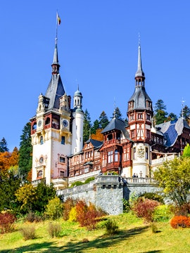 Peles Castle in Sinaia, Romania, with ornate towers and autumn foliage.