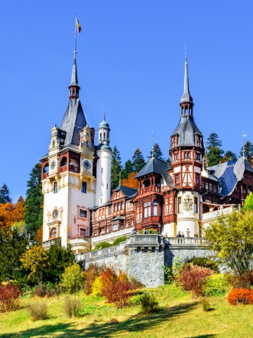 Peles Castle in Sinaia, Romania, with ornate towers and autumn foliage.