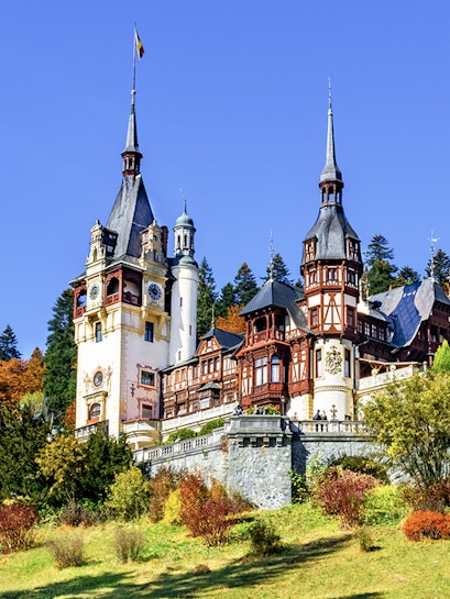 Peles Castle in Sinaia, Romania, with ornate towers and autumn foliage.
