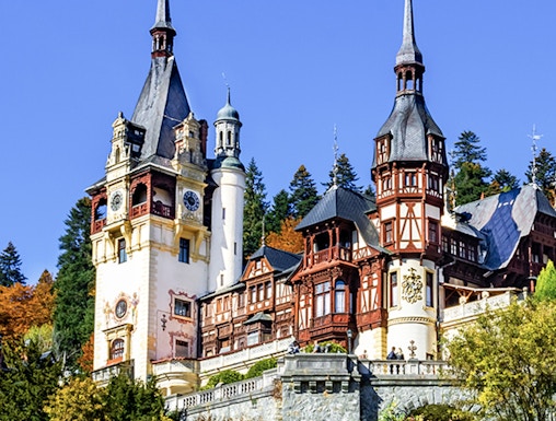 Peles Castle in Sinaia, Romania, with ornate towers and autumn foliage.