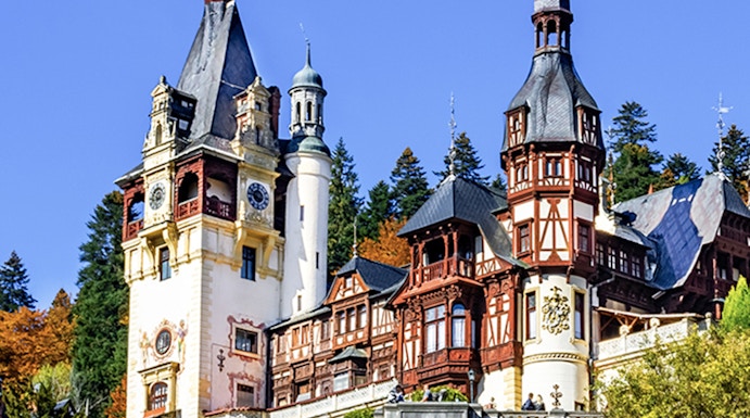 Peles Castle in Sinaia, Romania, with ornate towers and autumn foliage.