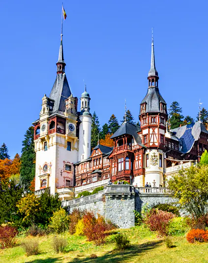 Peles Castle in Sinaia, Romania, with ornate towers and autumn foliage.