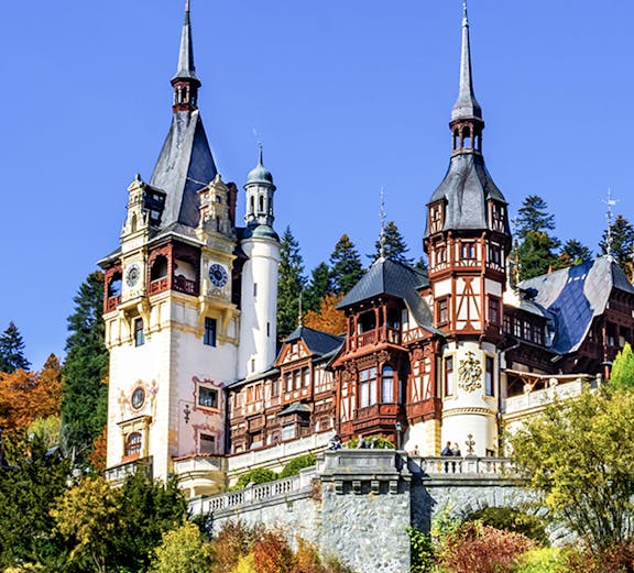 Peles Castle in Sinaia, Romania, with ornate towers and autumn foliage.