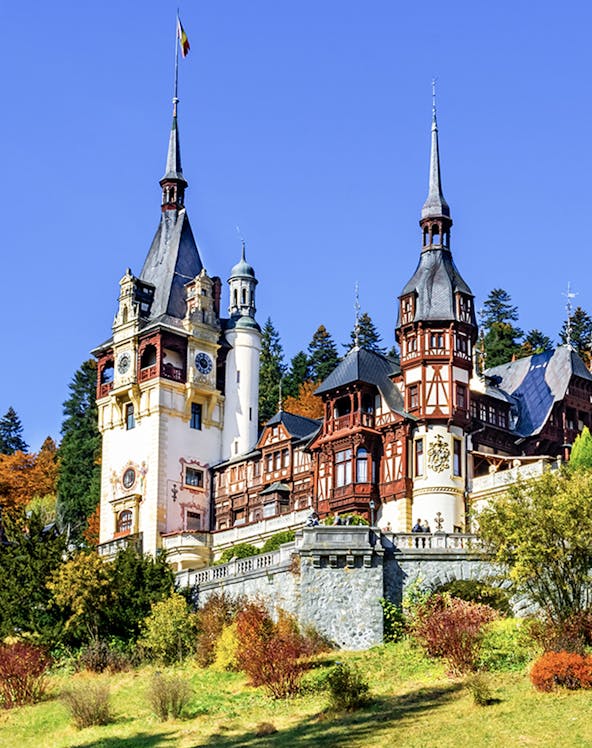 Peles Castle in Sinaia, Romania, with ornate towers and autumn foliage.