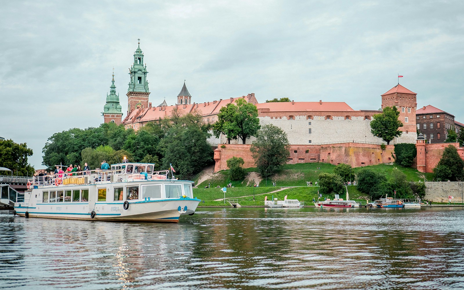 Vistula River cruise boat with tourists enjoying Krakow cityscape views.