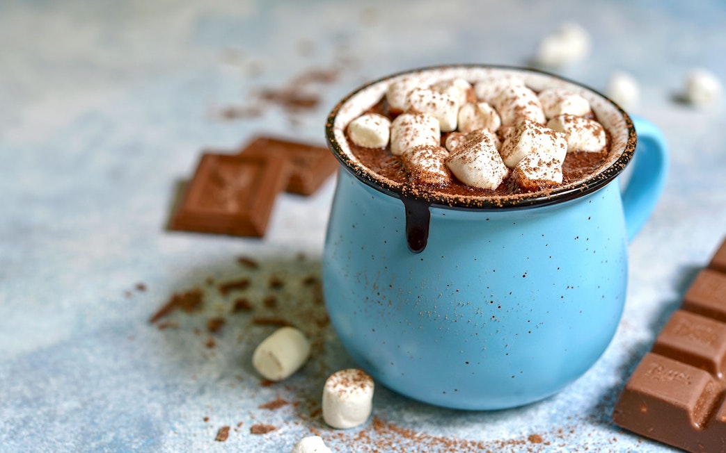 Hot chocolate with marshmallows in a blue mug, surrounded by chocolate pieces.