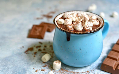 Hot chocolate with marshmallows in a blue mug, surrounded by chocolate pieces.