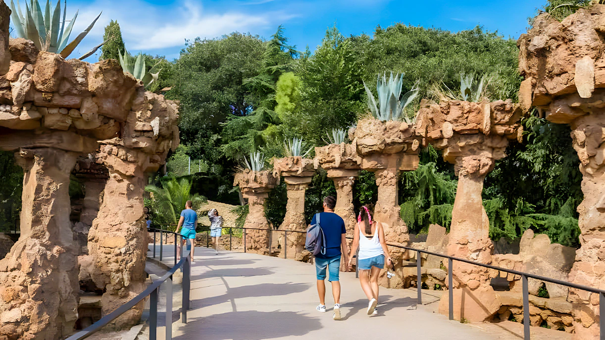 Visitors walking along a stone pathway in Park Güell, surrounded by unique rock columns and greenery.