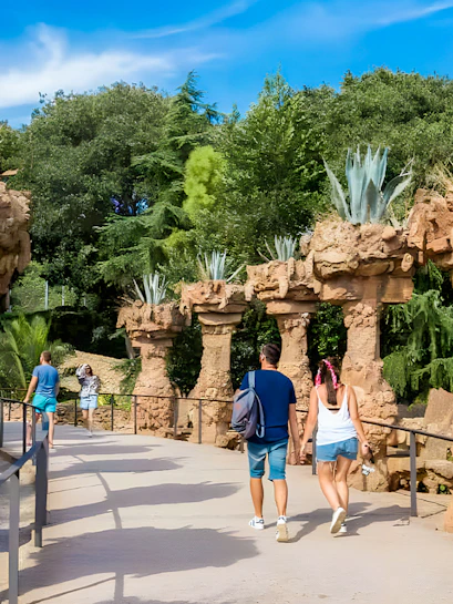 Park Güell stone pathway with visitors walking under unique rock columns.