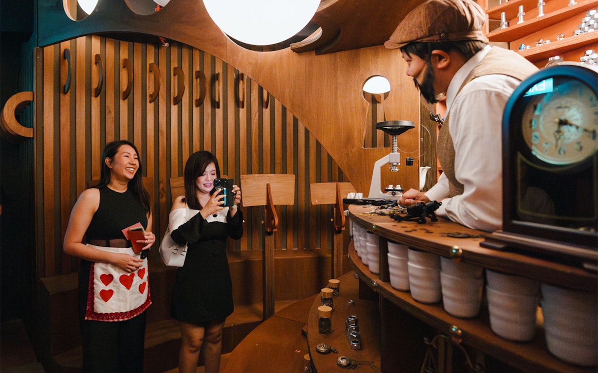 Guests interact with a costumed character at a whimsical service counter at Wonderland Upside Down.