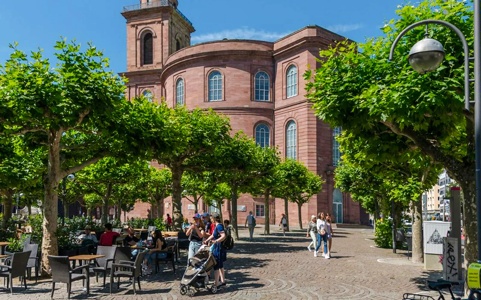 St. Paul's Church in Frankfurt with people walking and sitting under trees.