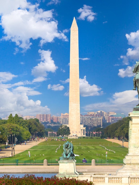 Washington Monument and statue at National Mall, Washington D.C., with clear sky and distant cityscape.