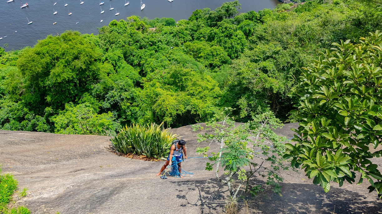 Climber ascending Sugarloaf Mountain with lush greenery and bay view, Rio de Janeiro, Brazil.