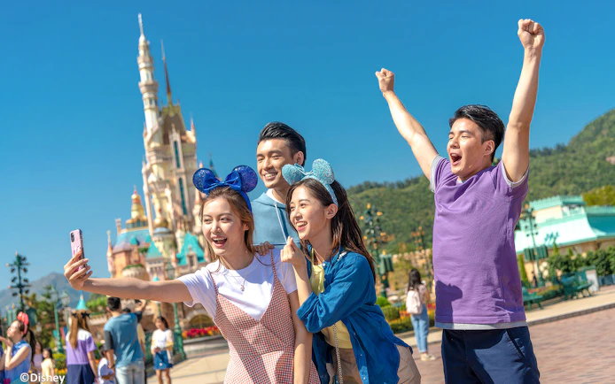 Friends taking selfie at Hong Kong Disneyland in front of castle.