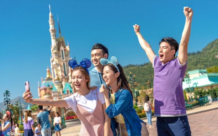 Friends taking selfie at Hong Kong Disneyland in front of castle.