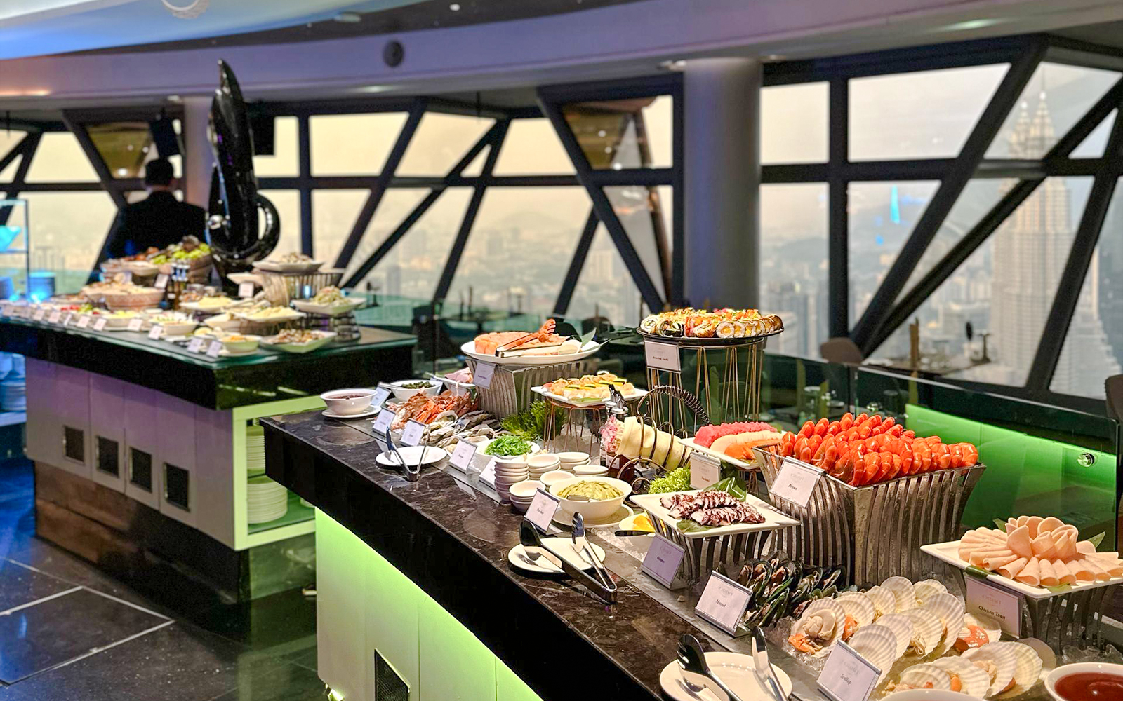 Buffet spread at ORBIT Revolving Restaurant in KL Tower with city view.