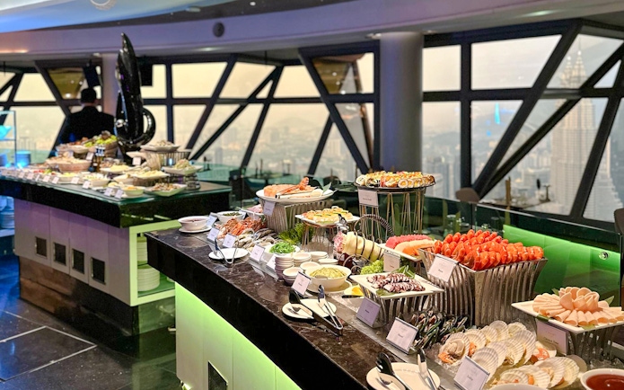 Buffet spread at ORBIT Revolving Restaurant in KL Tower with city view.