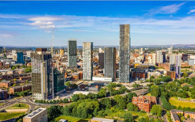Manchester skyline with modern skyscrapers and green spaces, viewed from above.