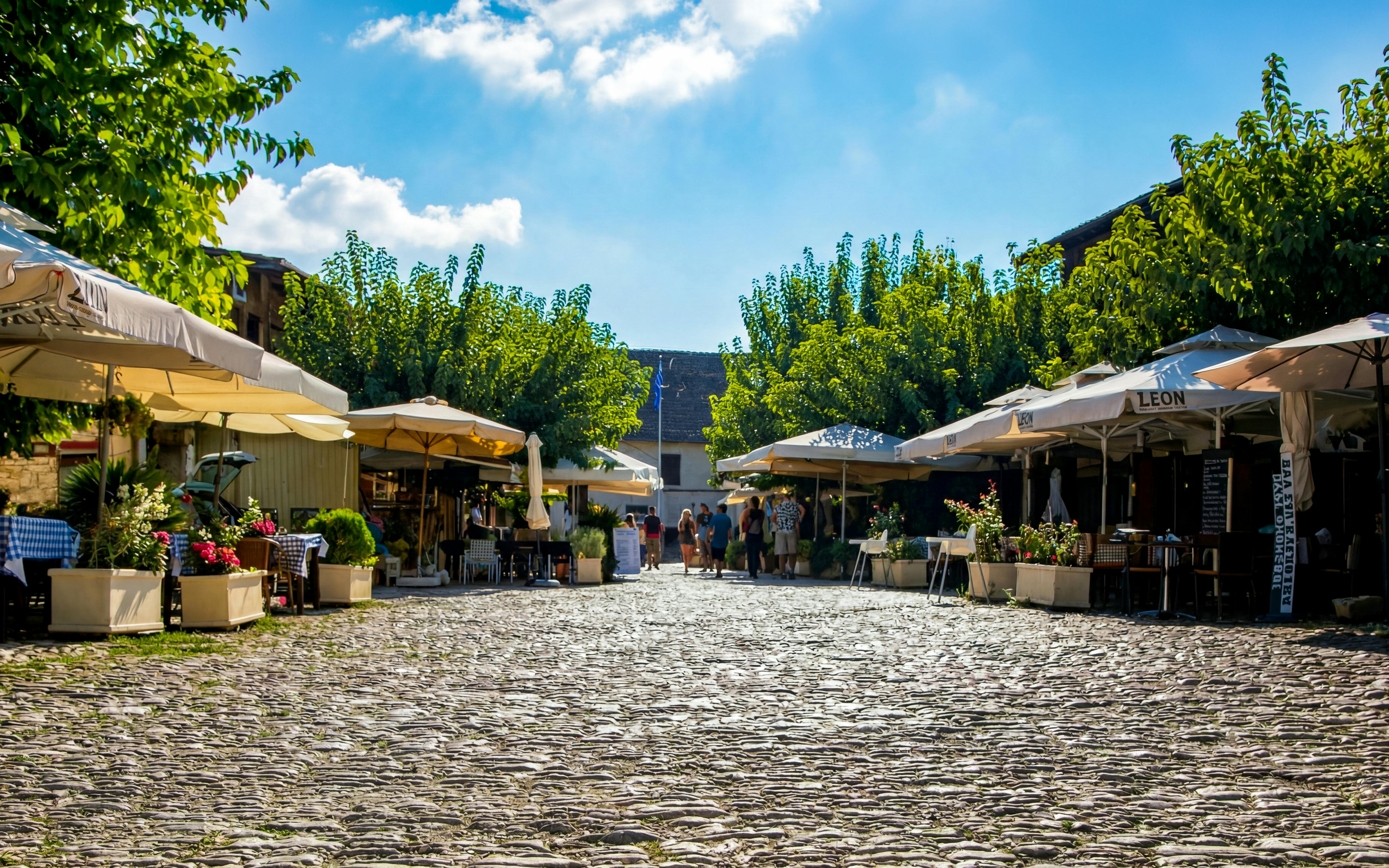 Cobblestone street in Omodos village with outdoor cafes and people strolling.