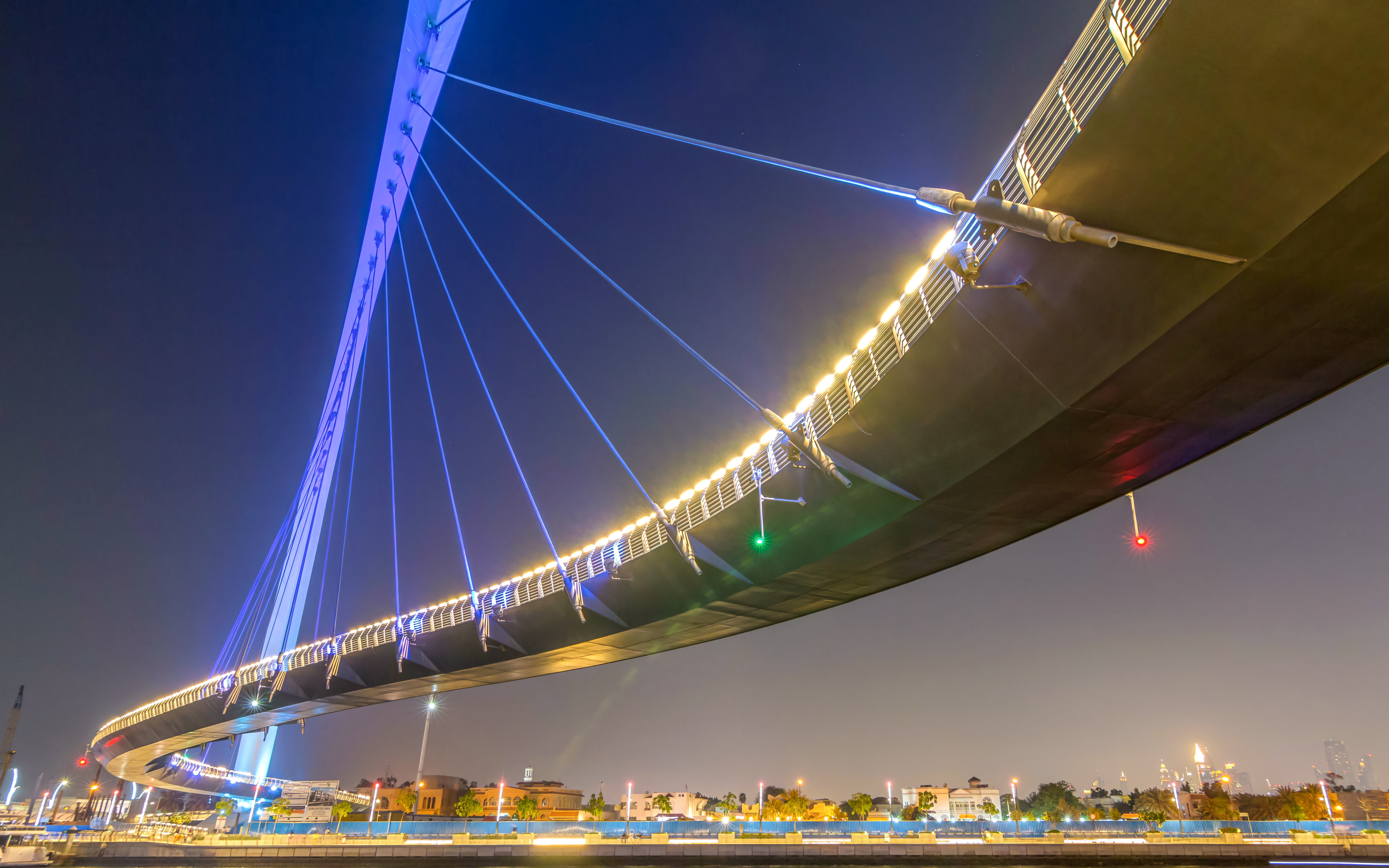 Dubai Canal bridge illuminated at night with city skyline in the background.