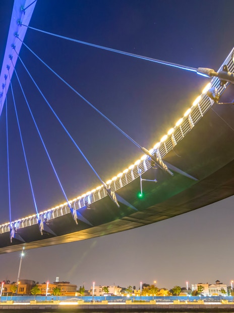Dubai Canal bridge illuminated at night with city skyline in the background.