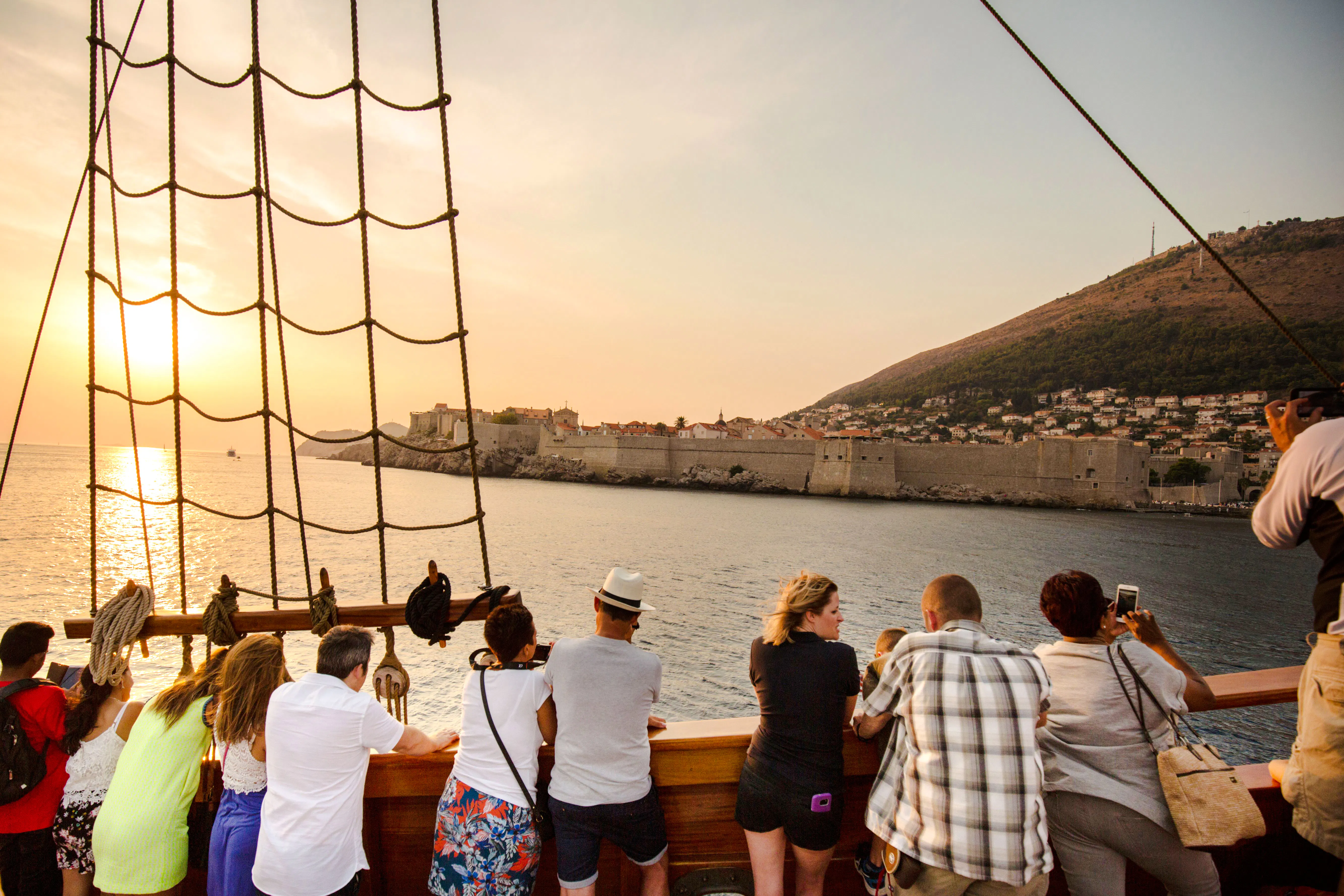 Tourists on a pirate ship cruise view Dubrovnik's Old Town at sunset.