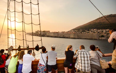 Tourists on a pirate ship cruise view Dubrovnik's Old Town at sunset.