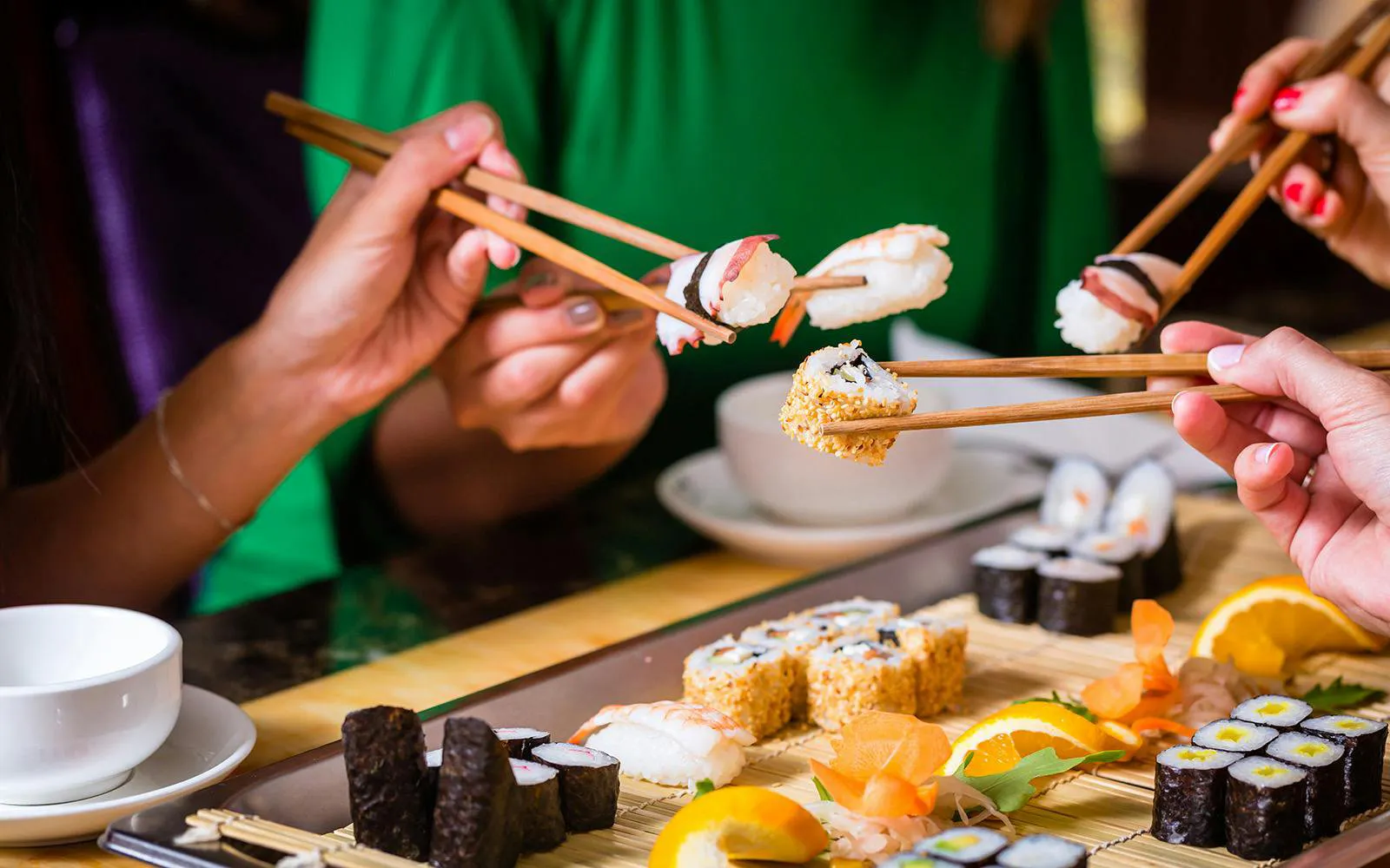 Young people using chopsticks to eat sushi in an Asian restaurant.