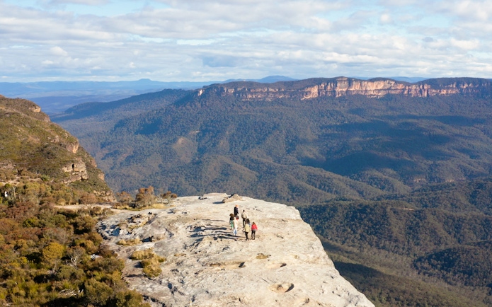 Group hiking on a cliff in Blue Mountains, Australia, with expansive forest views.