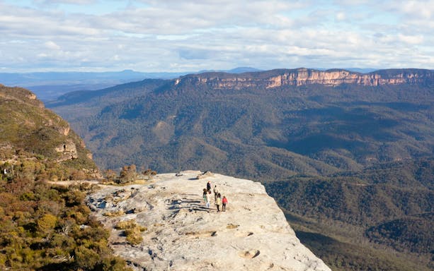 Group hiking on a cliff in Blue Mountains, Australia, with expansive forest views.