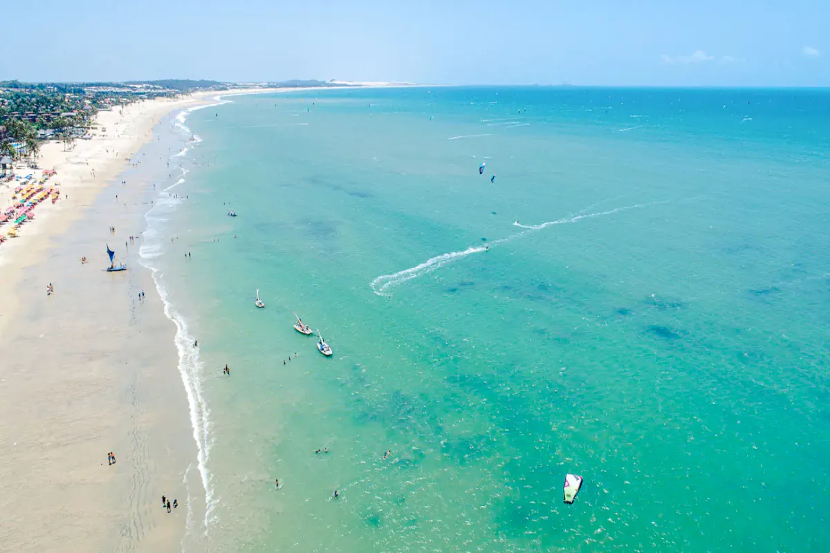 Cumbuco beach with kitesurfers and boats on turquoise water, Sao Paulo coastal adventure.