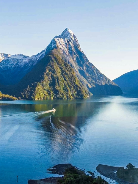 Cruise ship in Milford Sound fjords, New Zealand, with tourists enjoying canapes and champagne.
