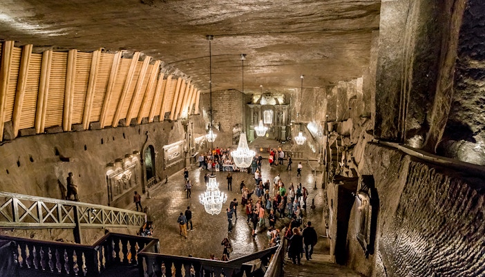 Visitors exploring the Wieliczka Salt Mine chamber with chandeliers and carved walls.