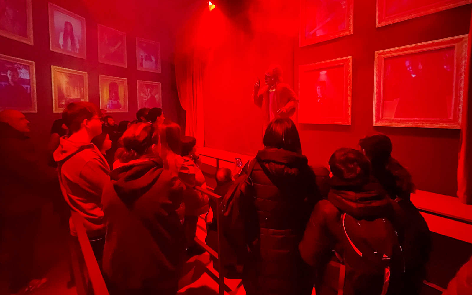 Group of tourists in a red-lit room at Hotel 666, viewing framed portraits and a performer.