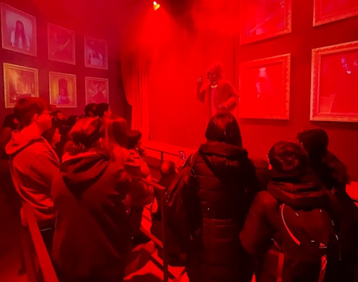 Group of tourists in a red-lit room at Hotel 666, viewing framed portraits and a performer.