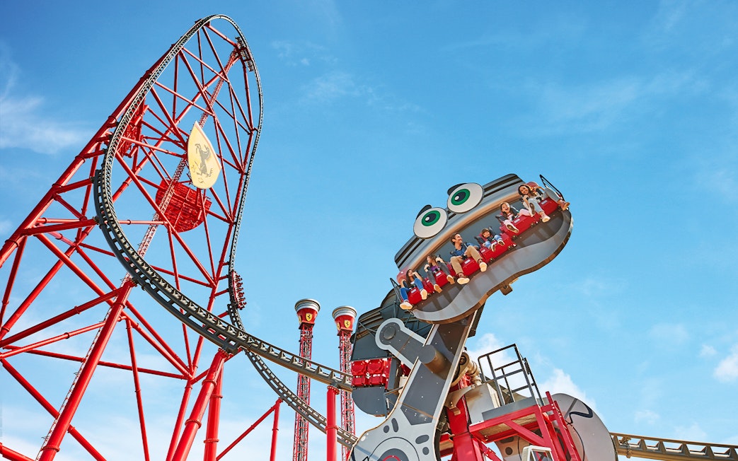 Roller coaster with riders at Ferrari Land, featuring a red track and blue sky.