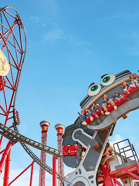 Roller coaster with riders at Ferrari Land, featuring a red track and blue sky.