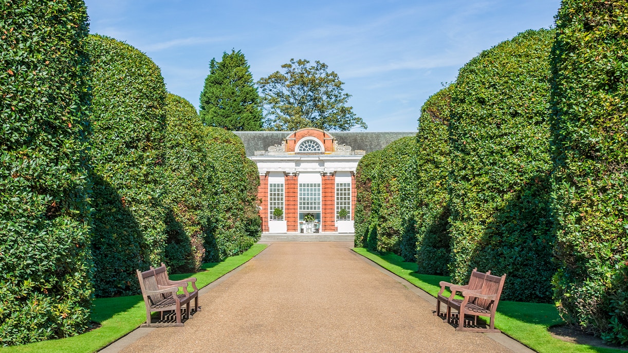 Tourists at the Orangery in Kensington Gardens, London, surrounded by historic architecture and lush greenery.