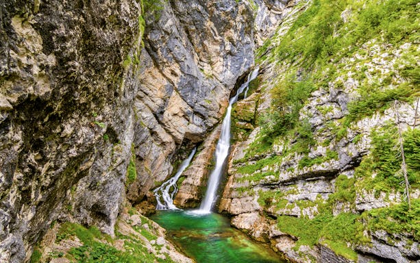 Slap Savica Waterfall cascading down rocky cliffs into a turquoise pool in Slovenia.