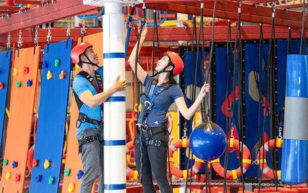 Participants navigating two-level elevated rope course indoors.