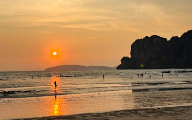 Sunset over Railay Beach with silhouettes of people and boats, Krabi.