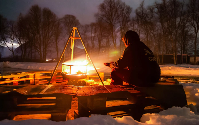 Person warming hands by campfire at Tromsø safari camp during aurora chase.