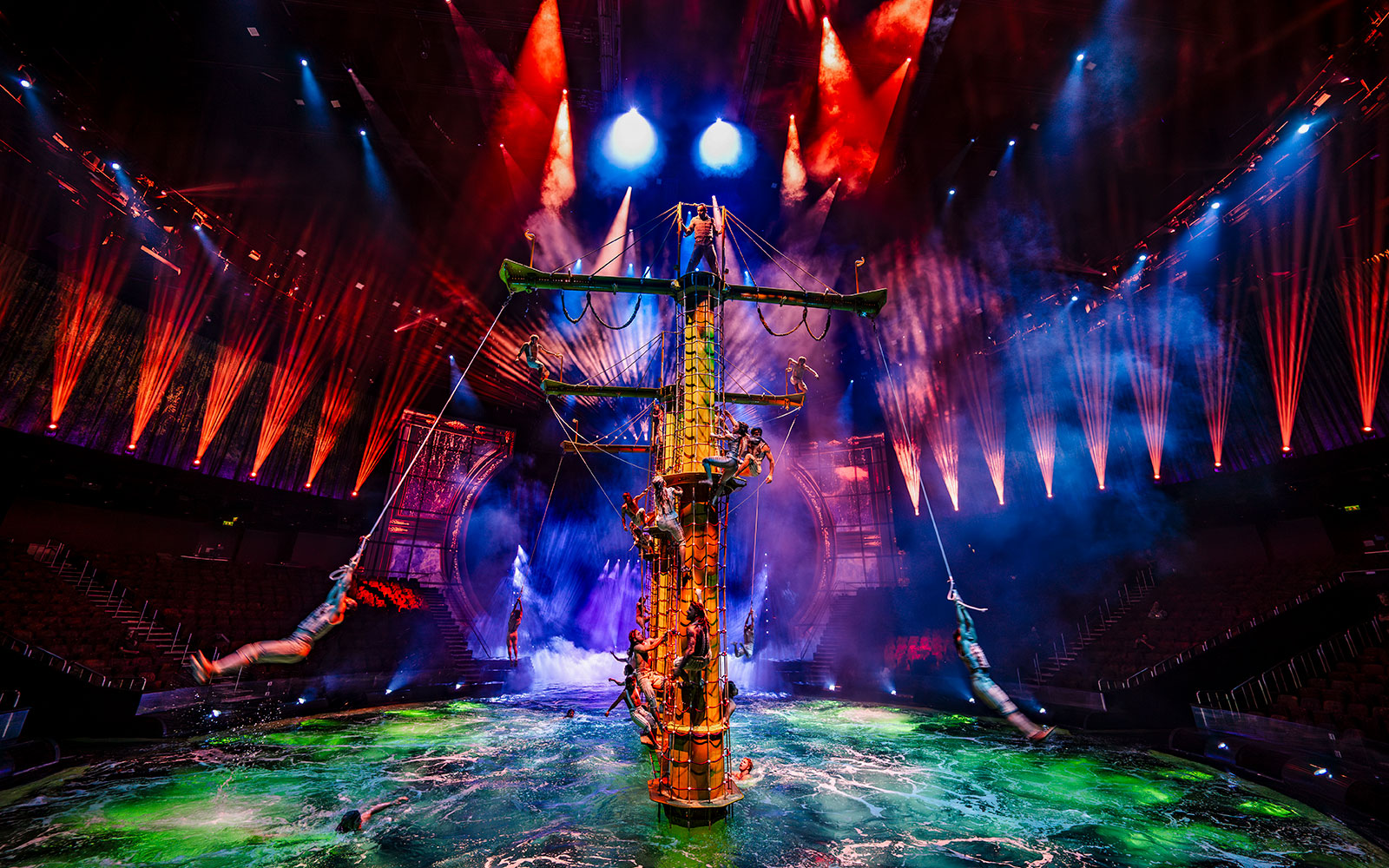 Performers on a ship mast during House of Dancing Water show with vibrant lights.