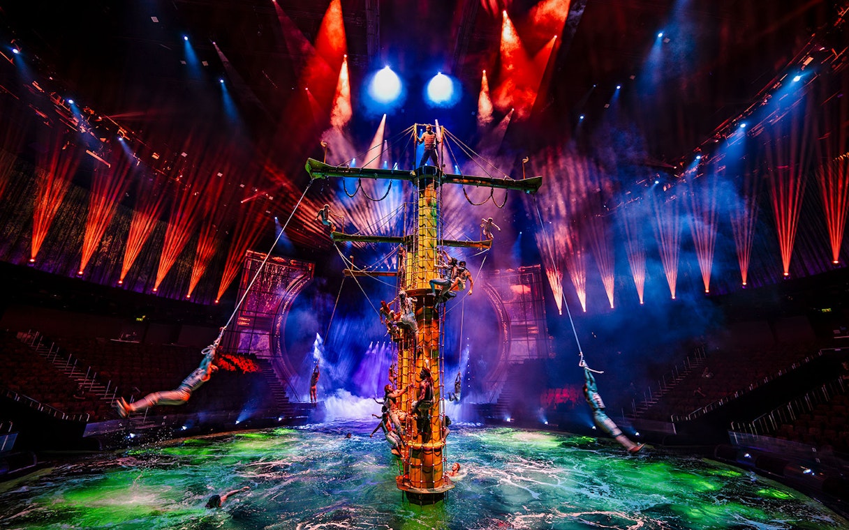 Performers on a ship mast during House of Dancing Water show with vibrant lights.
