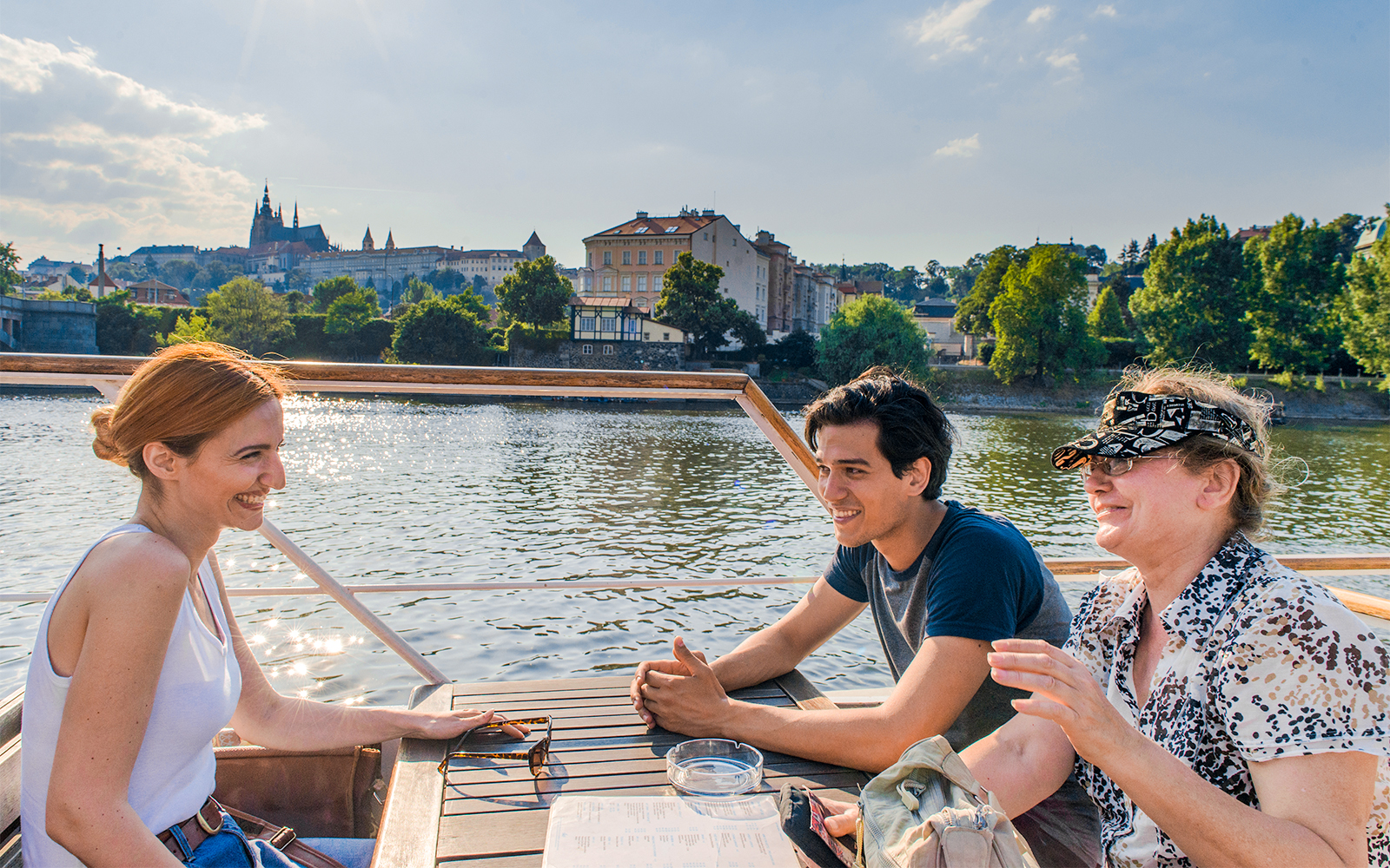 People enjoying a boat tour on the Vltava River with Prague Castle in the background.